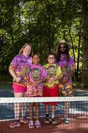 Family standing on a pickleball court holding paddles.
